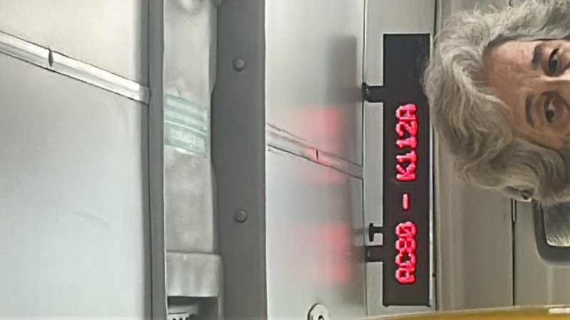 Partial view of an elderly woman beside a vertical red LED display on a metallic surface.