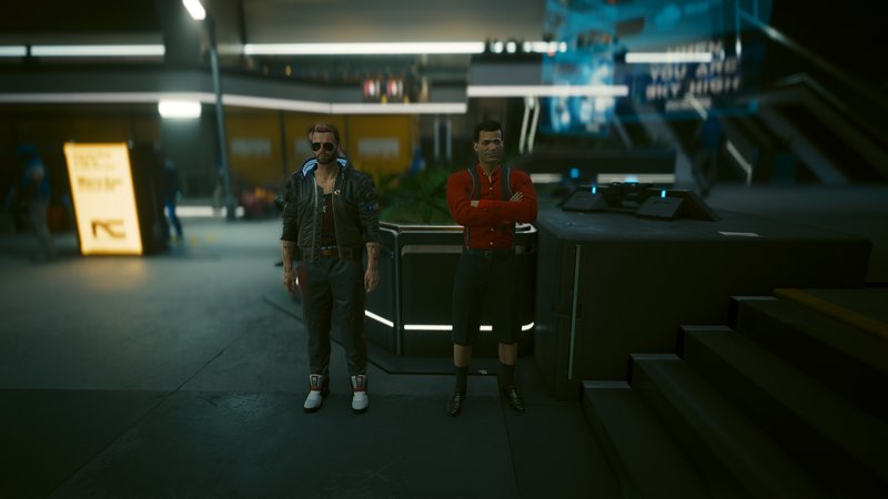 Two men in a neon-lit futuristic hallway stand near a sleek counter.