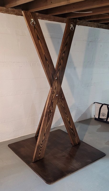 Handmade stained wooden X-frame ceiling support stand mounted to basement joists on a square dark...
