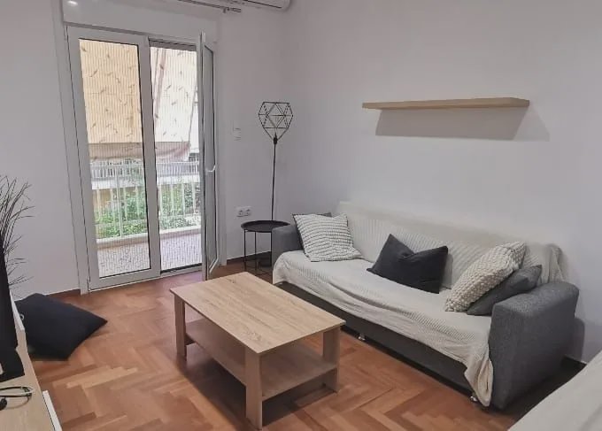 Bright minimalist small apartment living room with sofa, light wood coffee table, and sliding gla...