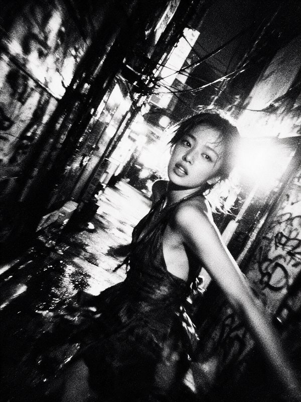 Grainy high contrast black and white portrait of a young woman posed in a graffiti-covered wet ci...