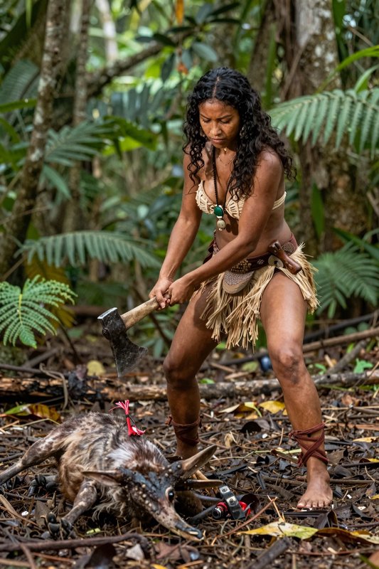 Indigenous amazonian hunter holds an axe standing over a fallen forest creature in dense rainforest