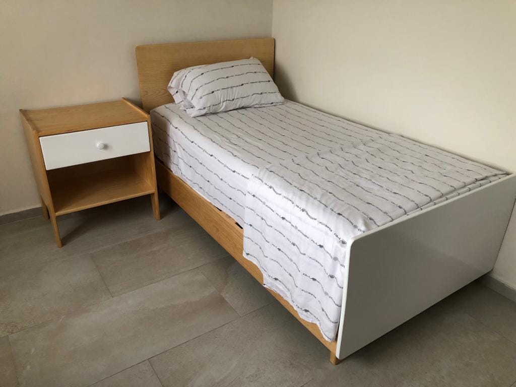 Single wooden-framed twin bed with striped bedding and matching nightstand.
