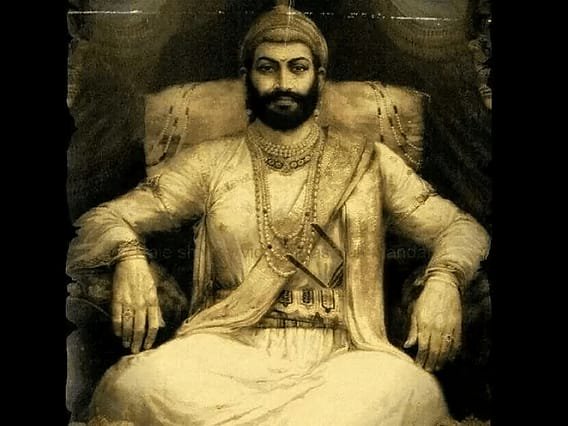 Sepia-toned portrait of a regal Indian king seated on a throne in traditional attire and jewelry.