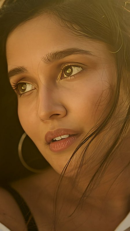 Close-up portrait of a young woman with warm lighting, brown eyes, and hoop earrings.