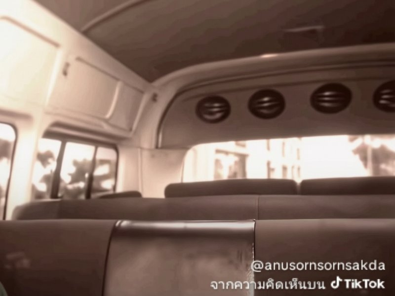 Inside a bus cabin with row seats, windows, and overhead vents in warm sepia tones