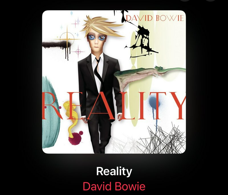 Anime-style illustration of a man in a black suit with large eyes, set against abstract splashes and the word REALITY in red.
