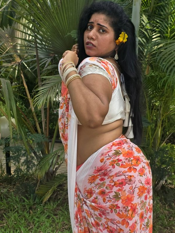 Woman in a white and orange floral saree posing in a tropical garden.