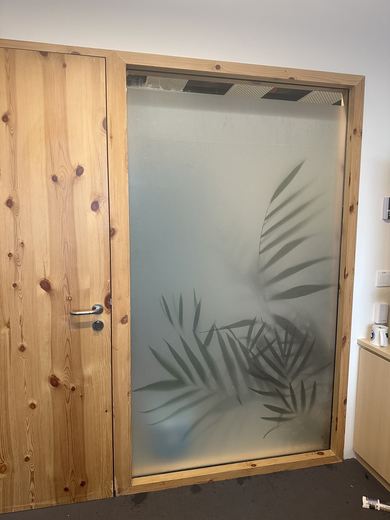 Frosted glass door with palm leaf botanical design framed by natural wood.