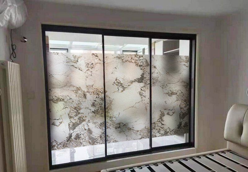 Modern bedroom with large sliding glass doors featuring marble-pattern privacy panels.