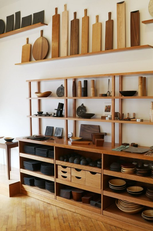 Light wood shelving unit displaying handcrafted wooden kitchenware, cutting boards, and artisanal...