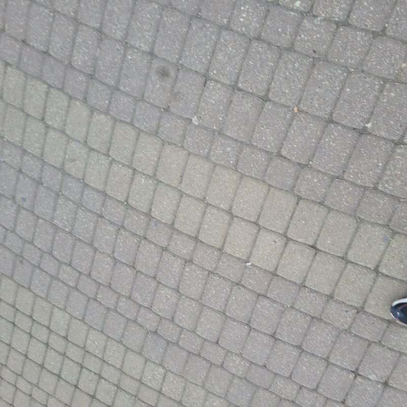 Close-up of a paved sidewalk with square concrete pavers in a diagonal grid and a partial sneaker...