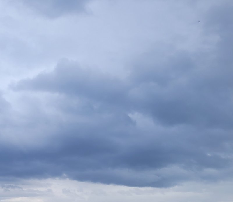 Overcast sky filled with dense layered cool-toned storm clouds, a tiny distant bird visible in th...