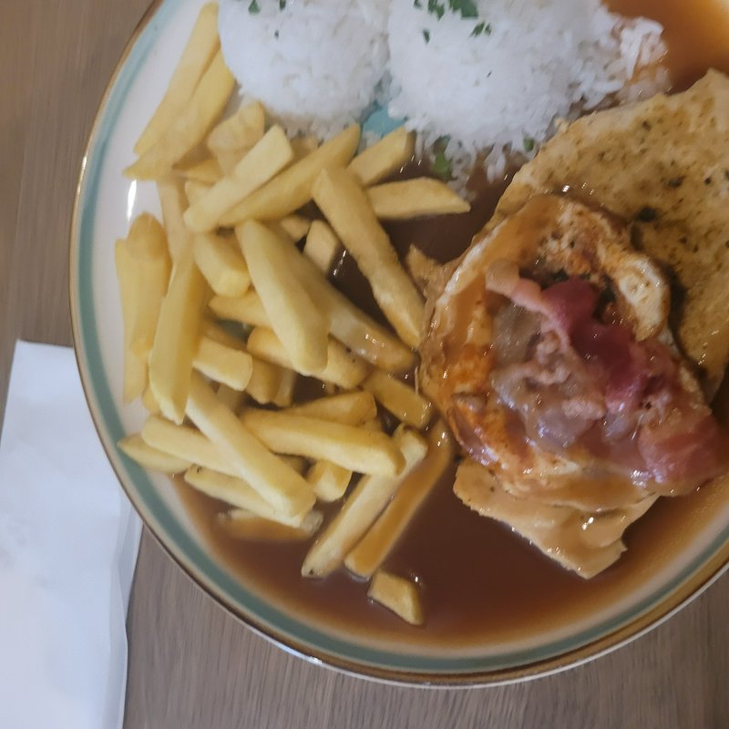 Top down view of a plated loco moco meal with fries, steamed rice, fried egg, bacon, and brown gr...