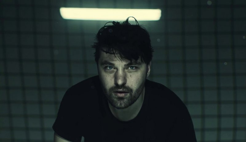 Moody male portrait in dim, blue-green lighting with a distressed expression.