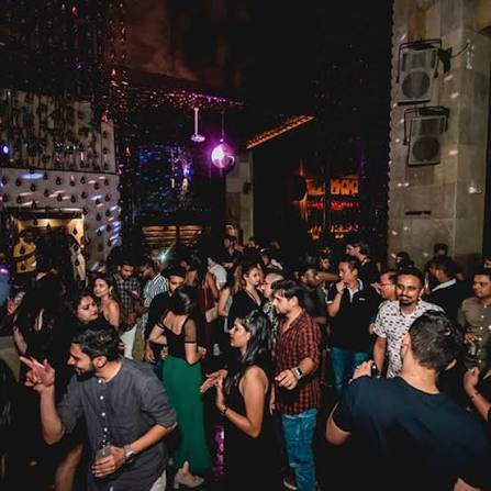 Crowded nightclub dance floor with colorful lights and a hanging disco ball.