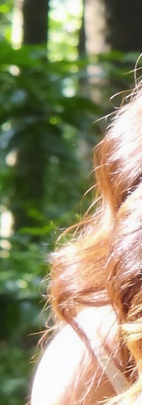 Close-up of red hair in the foreground with a blurred green forest background.