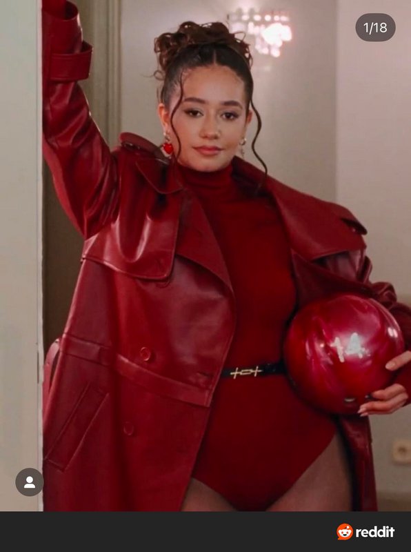 Woman in a glossy red leather coat and turtleneck posing with a red helmet in a bold, monochrome ...