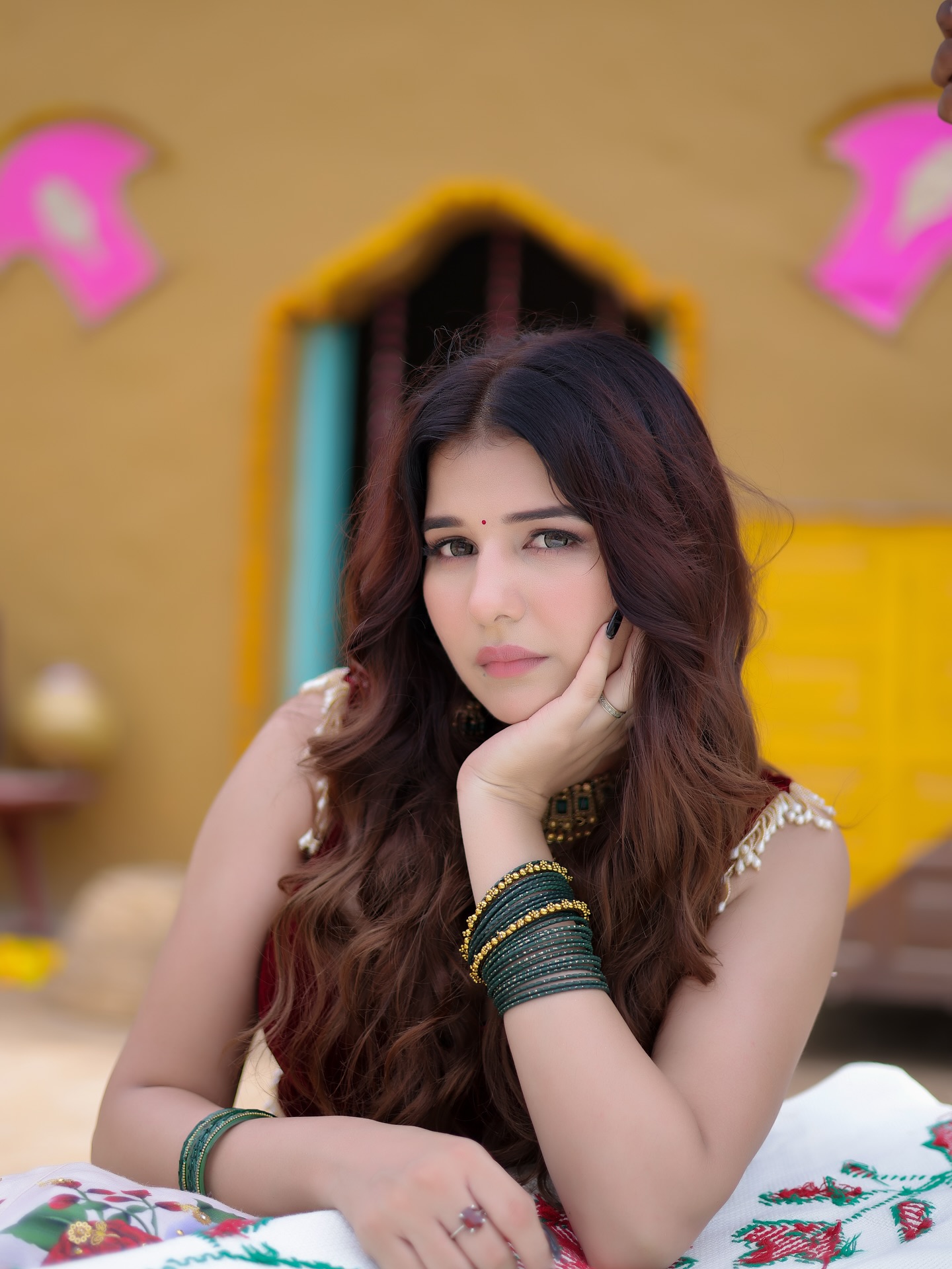 Portrait of a young Indian woman with long wavy hair, wearing green bangles and a bindi, resting her chin on her hand.