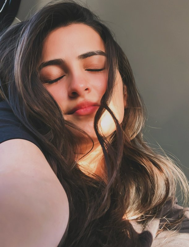 Close-up portrait of a woman with eyes closed, sunlit face and flowing hair.