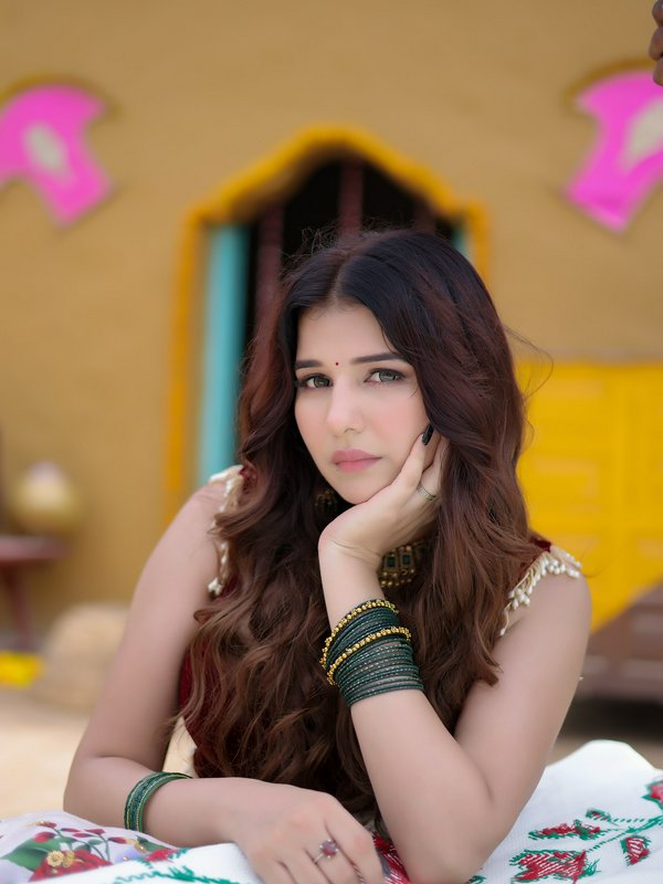 Portrait of a young Indian woman with long wavy hair, wearing green bangles and a bindi, resting her chin on her hand.