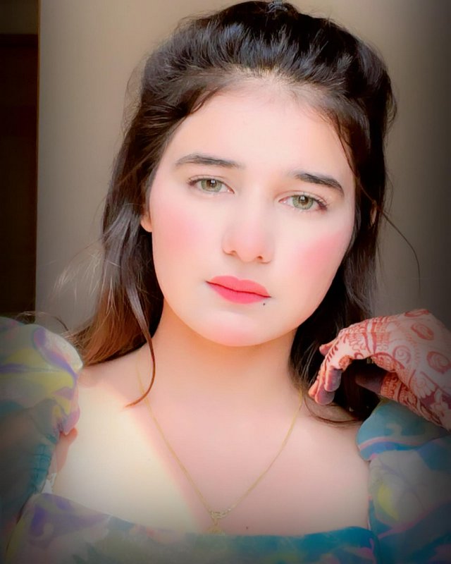 Portrait of a young woman with rosy cheeks and pink lips in pastel-toned attire.