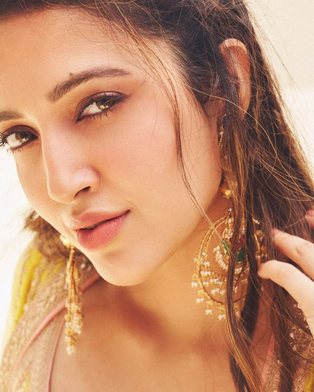 Close-up portrait of a woman with soft makeup, warm tones, and gold jewelry.
