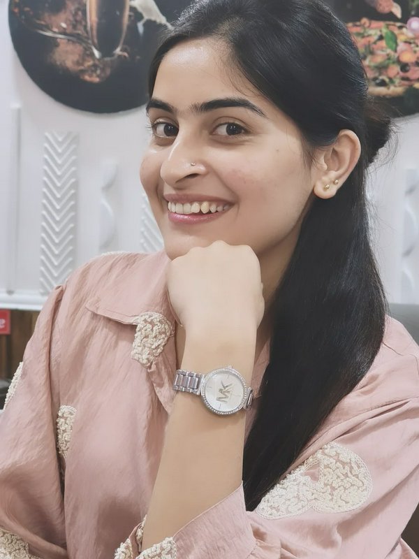 Smiling young woman with long dark hair wearing a pink blouse and a silver wristwatch.