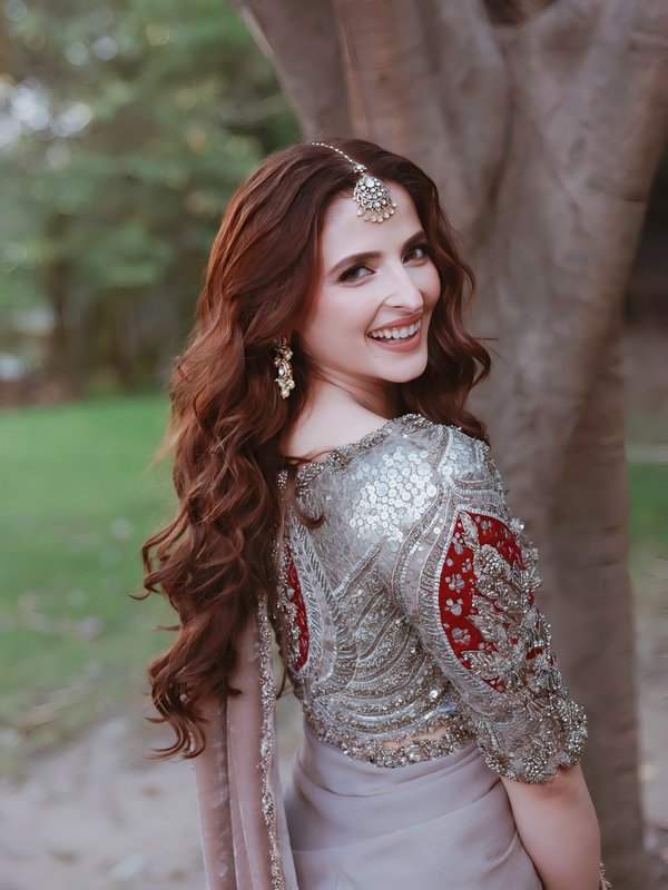 A smiling woman in a silver heavily embellished blouse with red embroidery, wearing jewelry outdo...