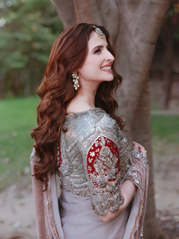 Smiling woman in a silver-embroidered traditional outfit with red panels and ornate jewelry outdo...
