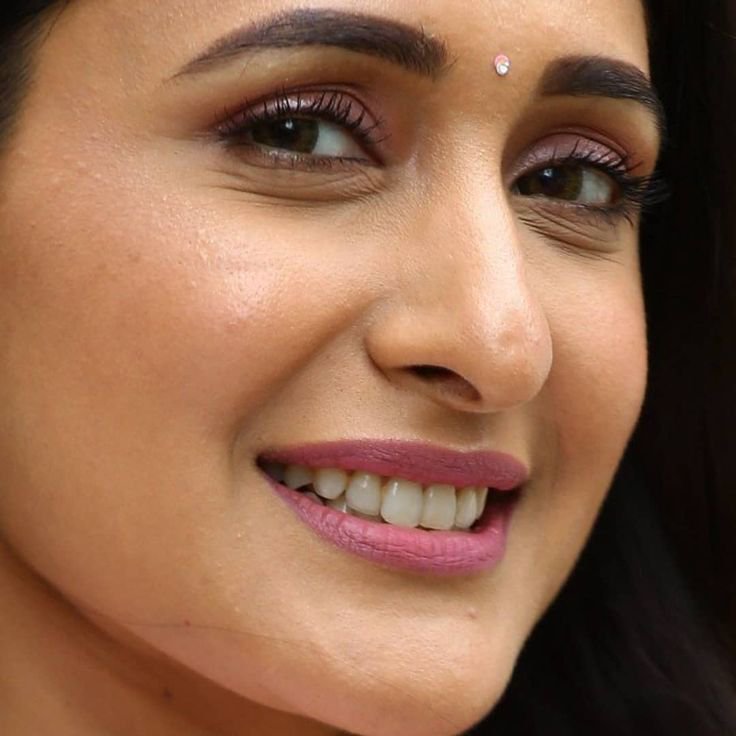 Close-up of a smiling woman with pink lipstick and a small bindi.