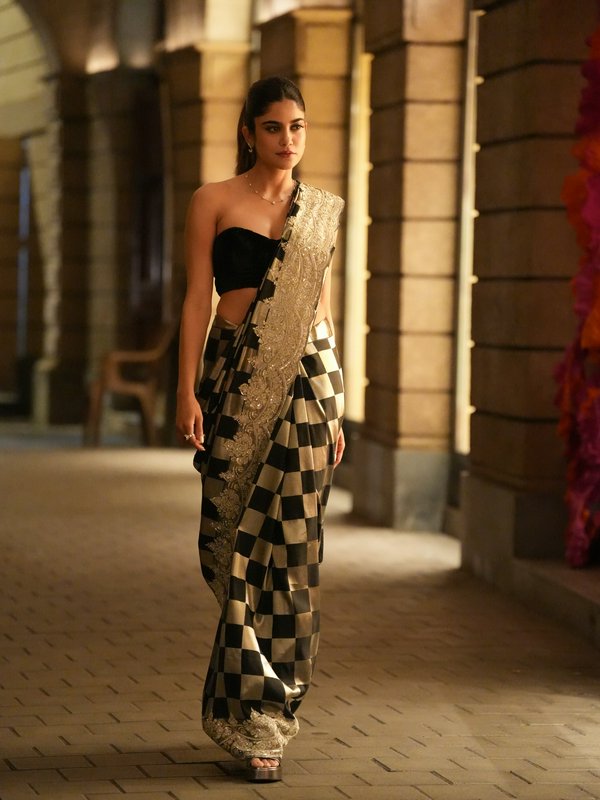 Young model walking in a luxury black and gold checkered embroidered designer saree in a warm lit...