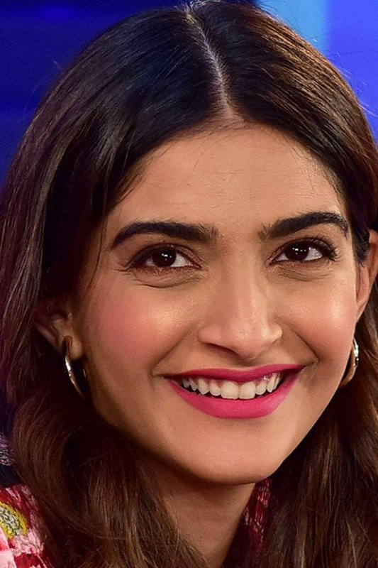 Close-up portrait of actress Sonam Kapoor smiling, wearing pink lipstick and gold hoop earrings a...
