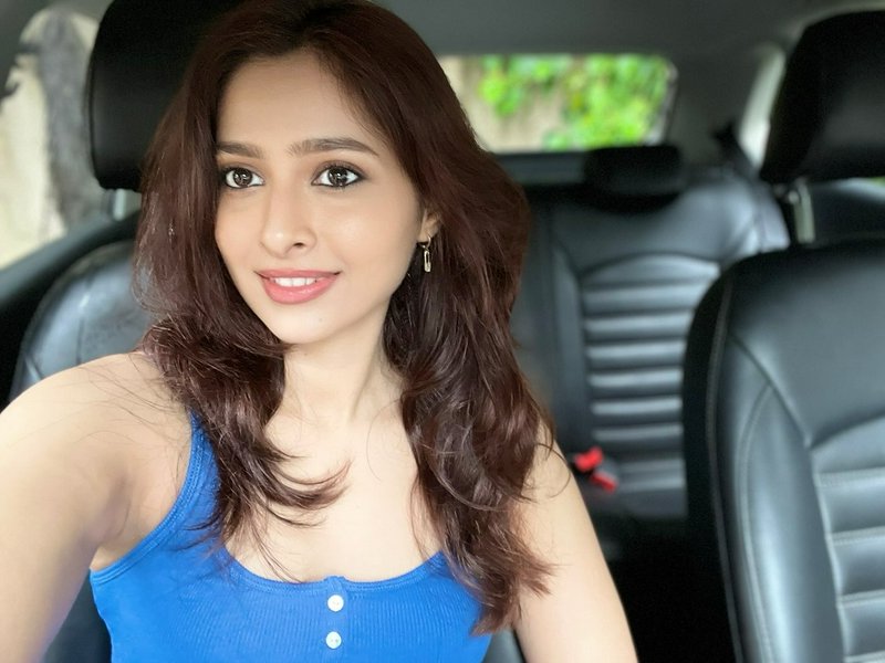 Smiling young South Asian woman takes a casual selfie from a car front seat, wearing a bright blu...