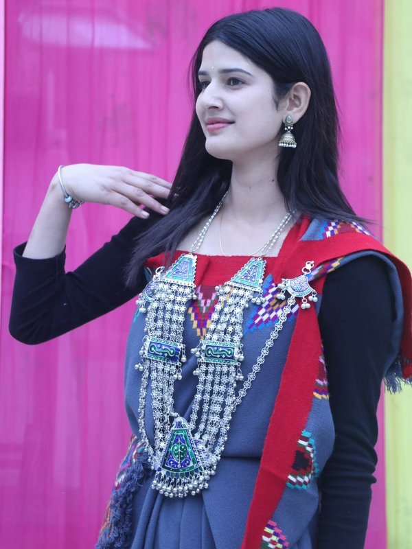 Young South Asian woman in traditional ethnic wear with ornate silver jewelry, posed against a br...