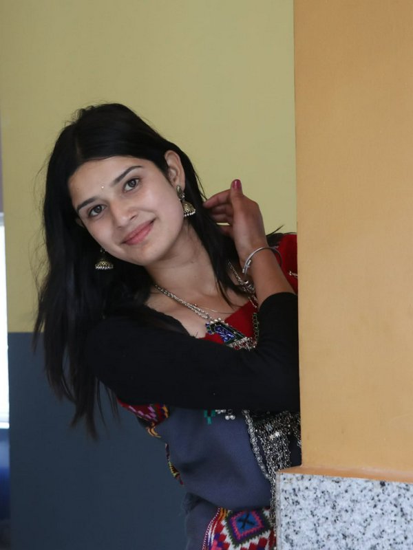 Smiling young South Asian woman in traditional embroidered attire peeks playfully from beside an ...