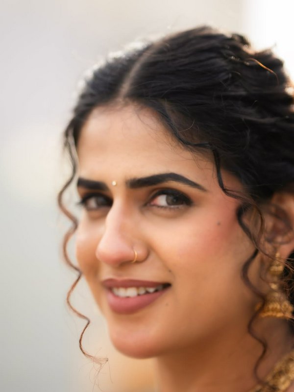 Close-up portrait of a smiling South Asian woman wearing traditional gold jewelry, a bindi, and l...