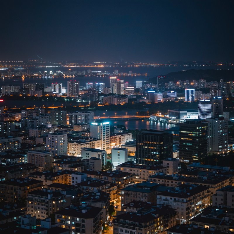 Nighttime city skyline with illuminated skyscrapers and a river running through the urban core.