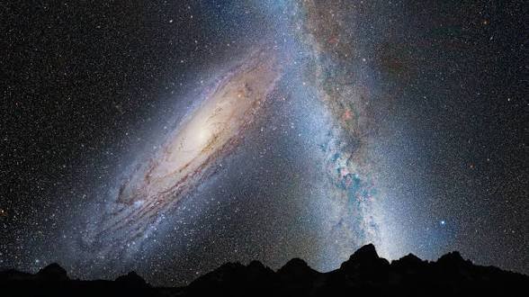 Night sky over jagged mountains with a bright Milky Way and a distant spiral galaxy.