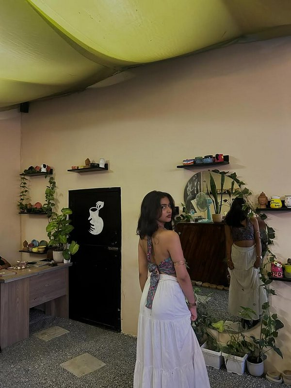 Boho-chic woman in a backless halter top and white maxi skirt in a plant-filled boutique.