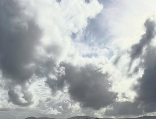 Dramatic cloudy sky with dark storm clouds over a distant hill horizon.