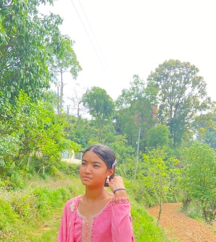 Young girl in a pink traditional dress standing in a green rural landscape.