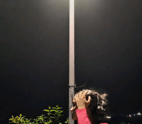 Viral optical illusion: a girl’s head appears split by a metal pole at night, hand on her head ag...