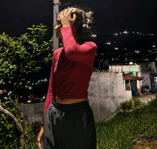 Young woman in a red cropped top touches her hair while overlooking a hilly residential neighborh...