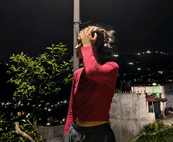 Profile view of young woman touching her hair, standing on a balcony overlooking a lit hillside t...