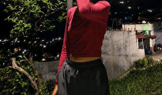 Cropped shot of a person in a maroon long-sleeve crop top standing on a grassy hillside overlooki...