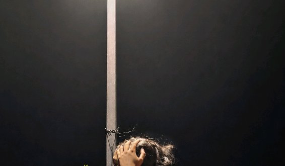 Person holding their head in distress, positioned next to a vertical pole against a dark minimalist background.