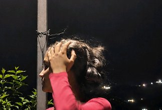 Profile view of a woman in a pink top running her hands through windblown curly hair outdoors at ...