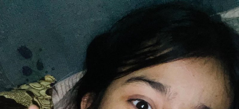 Partial close-up selfie of a person with dark hair lying against a teal bed sheet, looking toward...