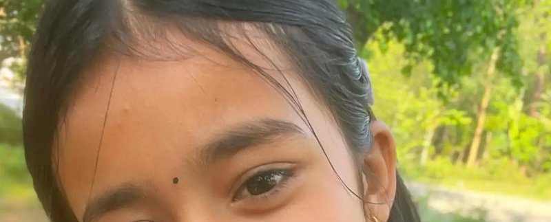 Close-up partial portrait of a South Asian woman with a bindi, posed outdoors in a sunlit green p...